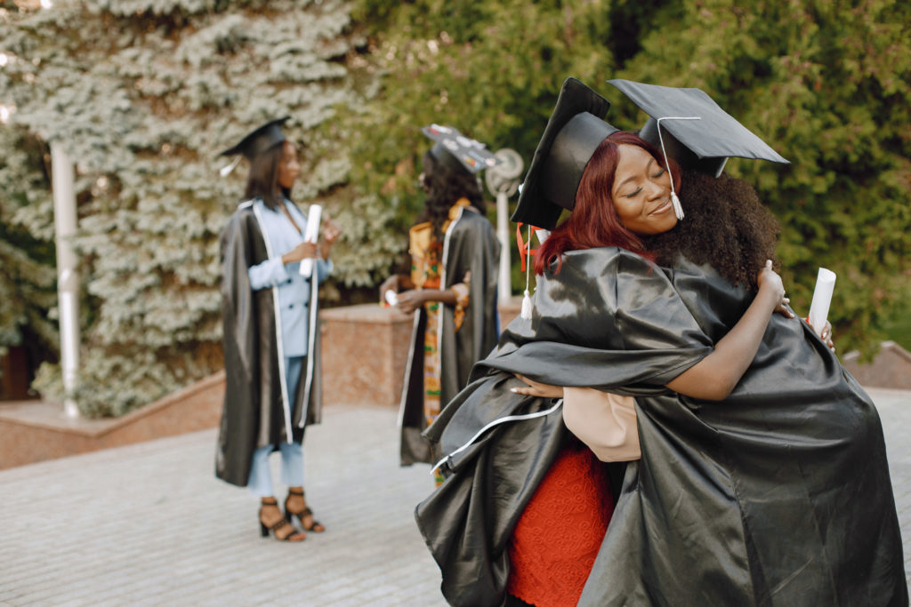 Two excited african american female students hugging at their gr